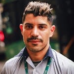Close-up portrait of a man with short hair wearing a lanyard outdoors. Natural light.